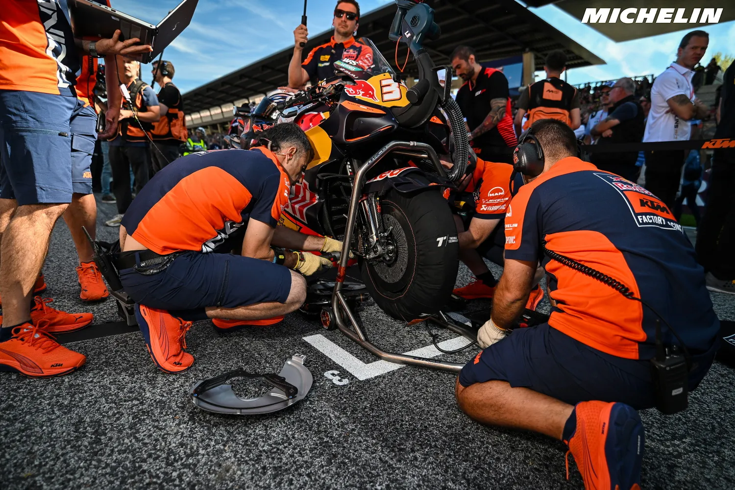Des mécaniciens KTM en orange préparent une moto sur la grille de départ